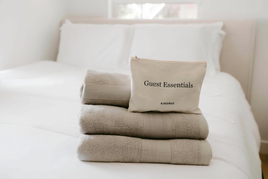 Kindred guest essentials kit placed on neatly folded towels atop a crisp white bed, highlighting the thoughtful amenities provided for a seamless home swapping experience.