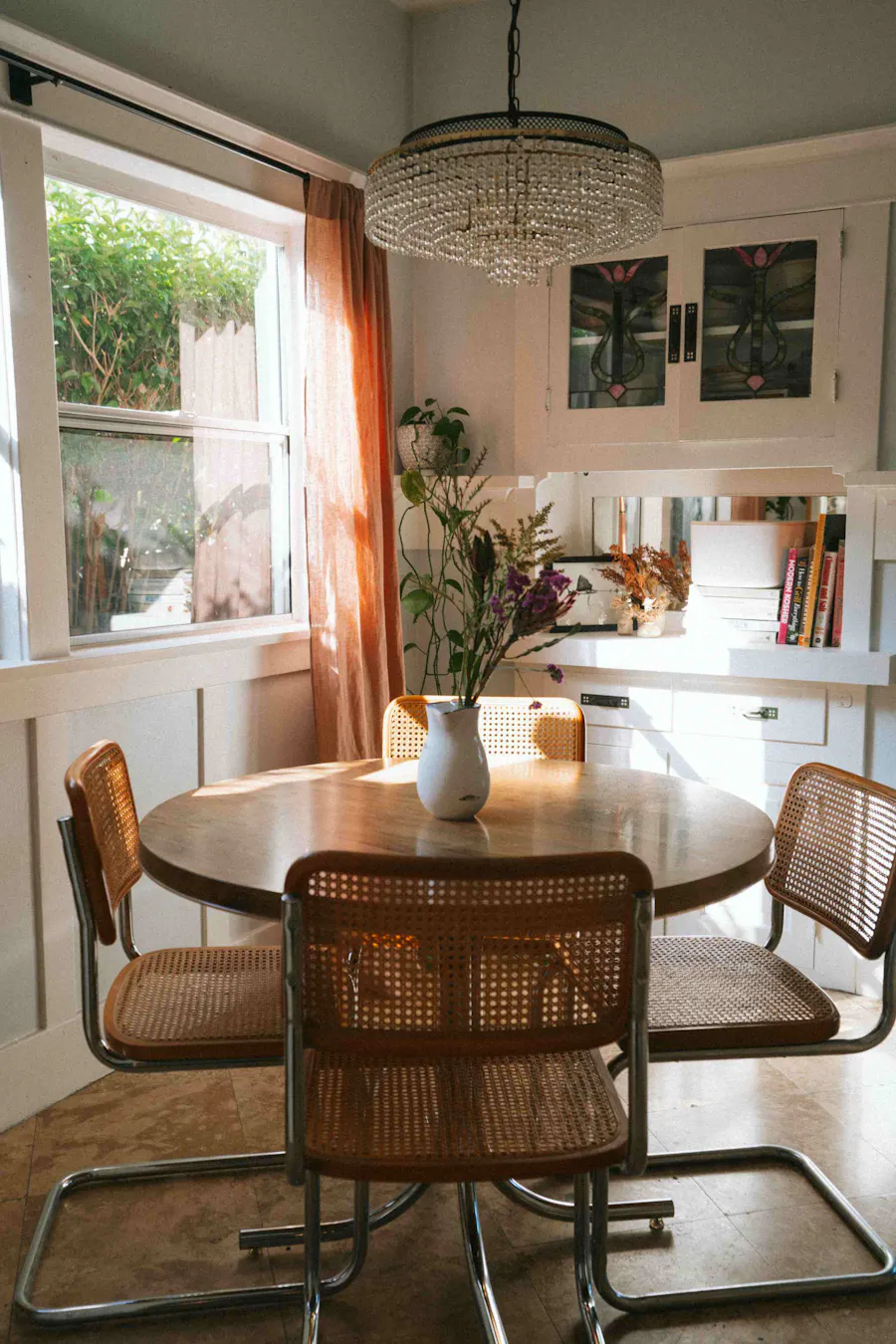 Charming dining area with a wooden table, woven chairs, and a crystal chandelier, bathed in natural light and adorned with fresh flowers, creating a warm and inviting space for Kindred guests.