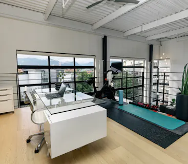 Modern loft workspace in a Kindred home, combining professional work setup with wellness amenities like a fitness area, perfect for maintaining work-life balance on the go.