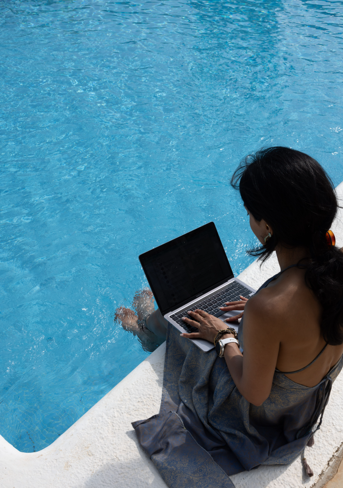 Woman working internationally from a beautifully decorated home office with large windows, lush green plants, and a modern desktop setup. Ideal for digital nomads seeking a productive and serene environment.