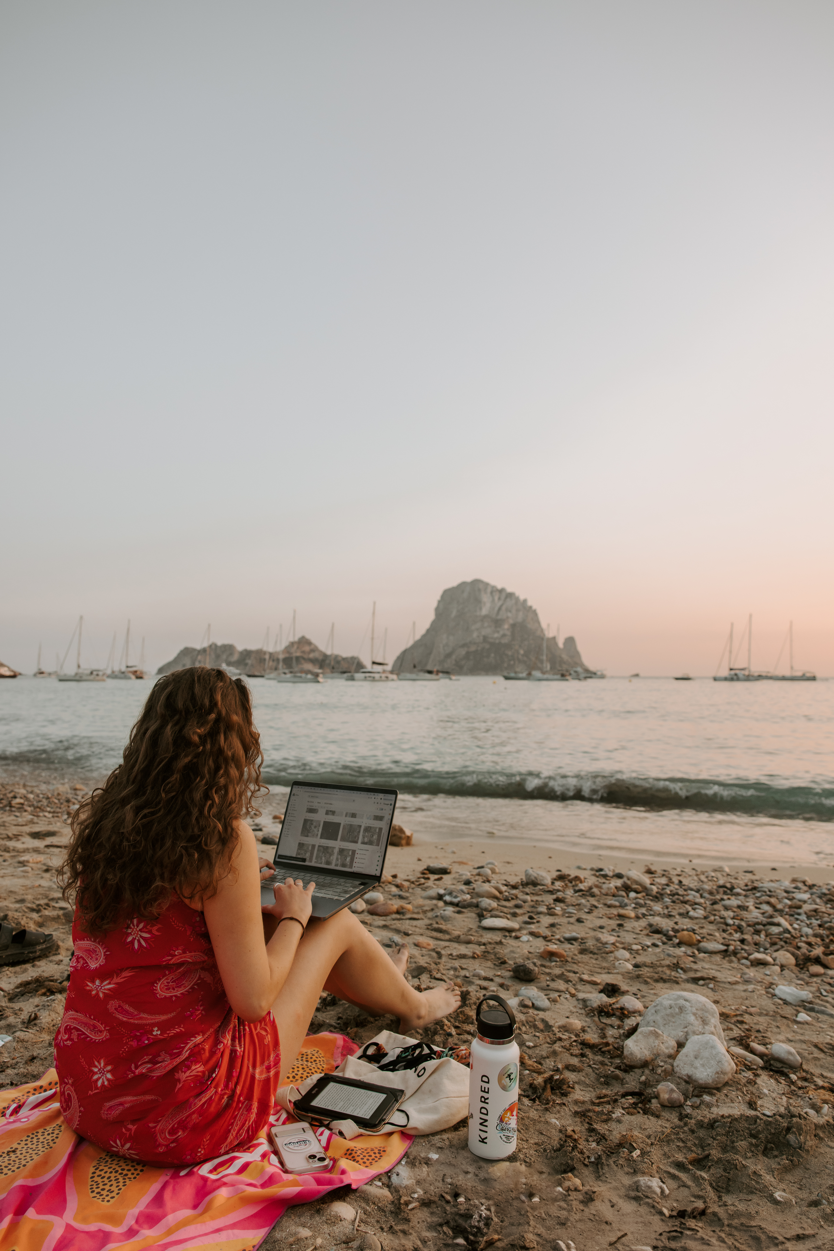 Woman working on a laptop by the beach, enjoying the ocean view and sunny weather. Perfect for digital nomads who value work-life balance, travel freedom, and inspiring surroundings.
