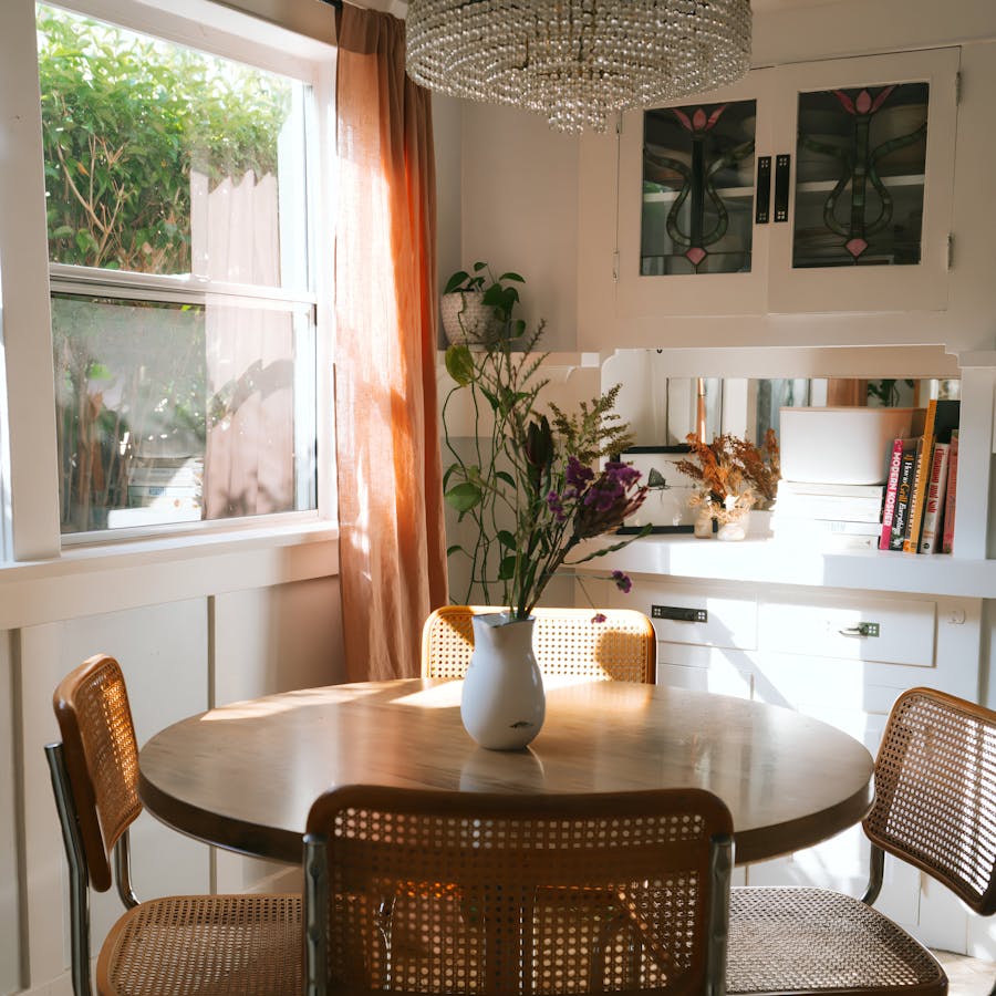 Sunlit dining nook with a round table, floral decor, and natural light, inviting relaxation and home-cooked meals. Enjoy routine-friendly Kindred home swaps—ideal for retirees and long-term travelers exploring new places without giving up daily comforts.