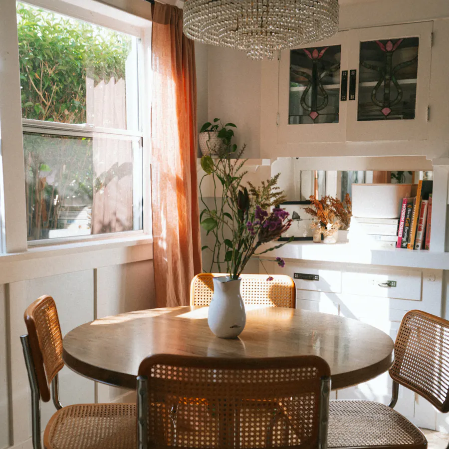 Sunlit dining nook with a round table, floral decor, and natural light, inviting relaxation and home-cooked meals. Enjoy routine-friendly Kindred home swaps—ideal for retirees and long-term travelers exploring new places without giving up daily comforts.