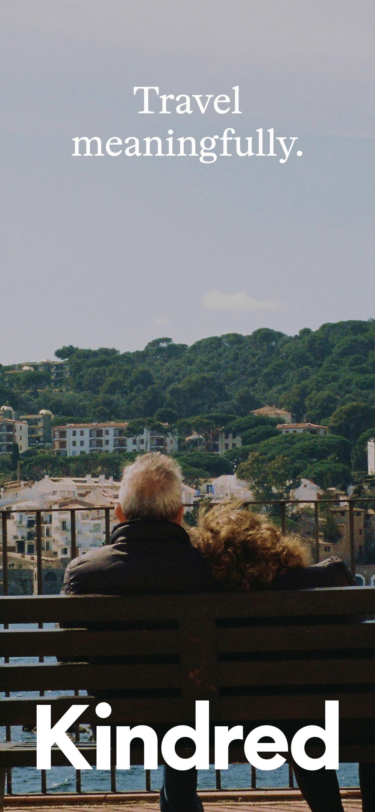 Older couple seated on a bench overlooking a coastal hillside village, with the words 'Travel meaningfully'—evoking the emotional depth and personal connections behind Kindred’s home exchange community.