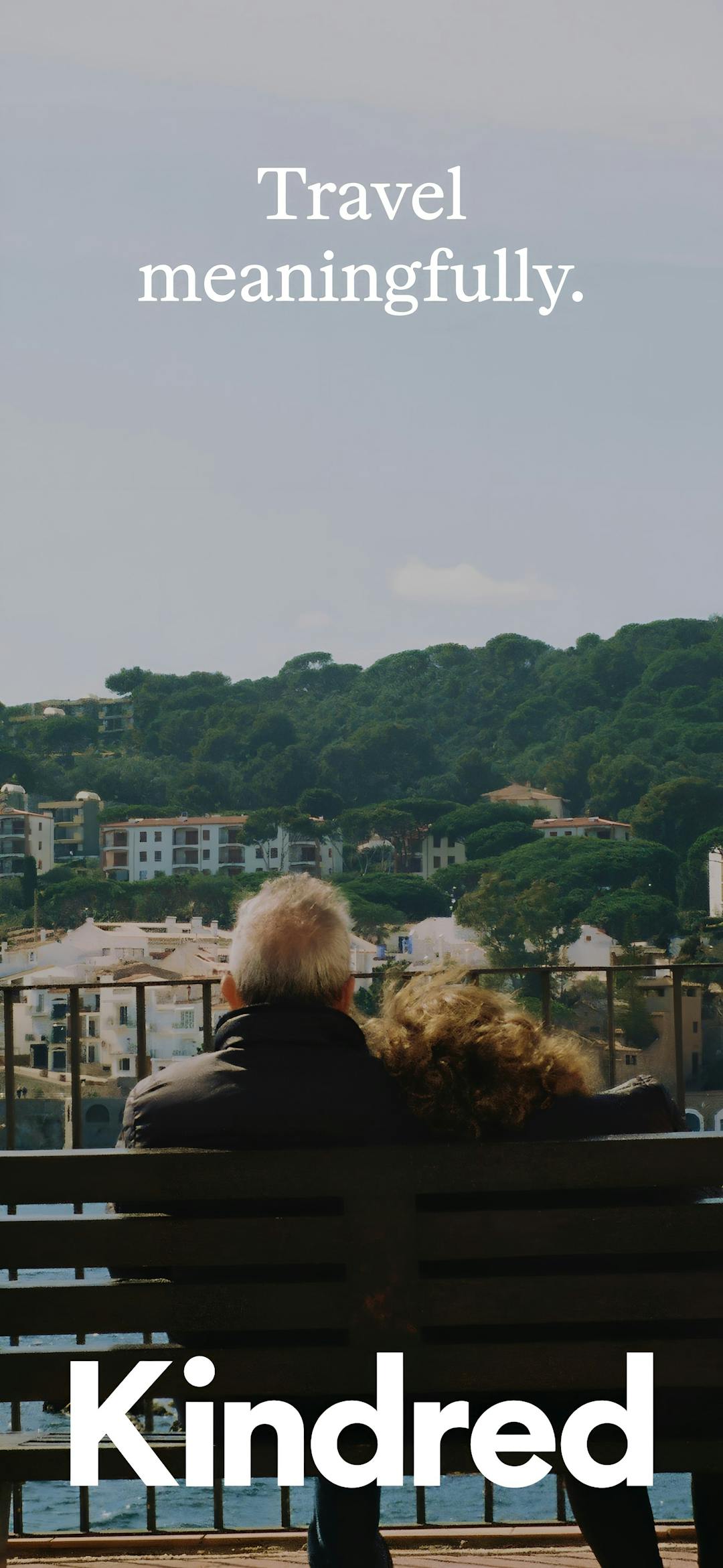 Older couple seated on a bench overlooking a coastal hillside village, with the words 'Travel meaningfully'—evoking the emotional depth and personal connections behind Kindred’s home exchange community.