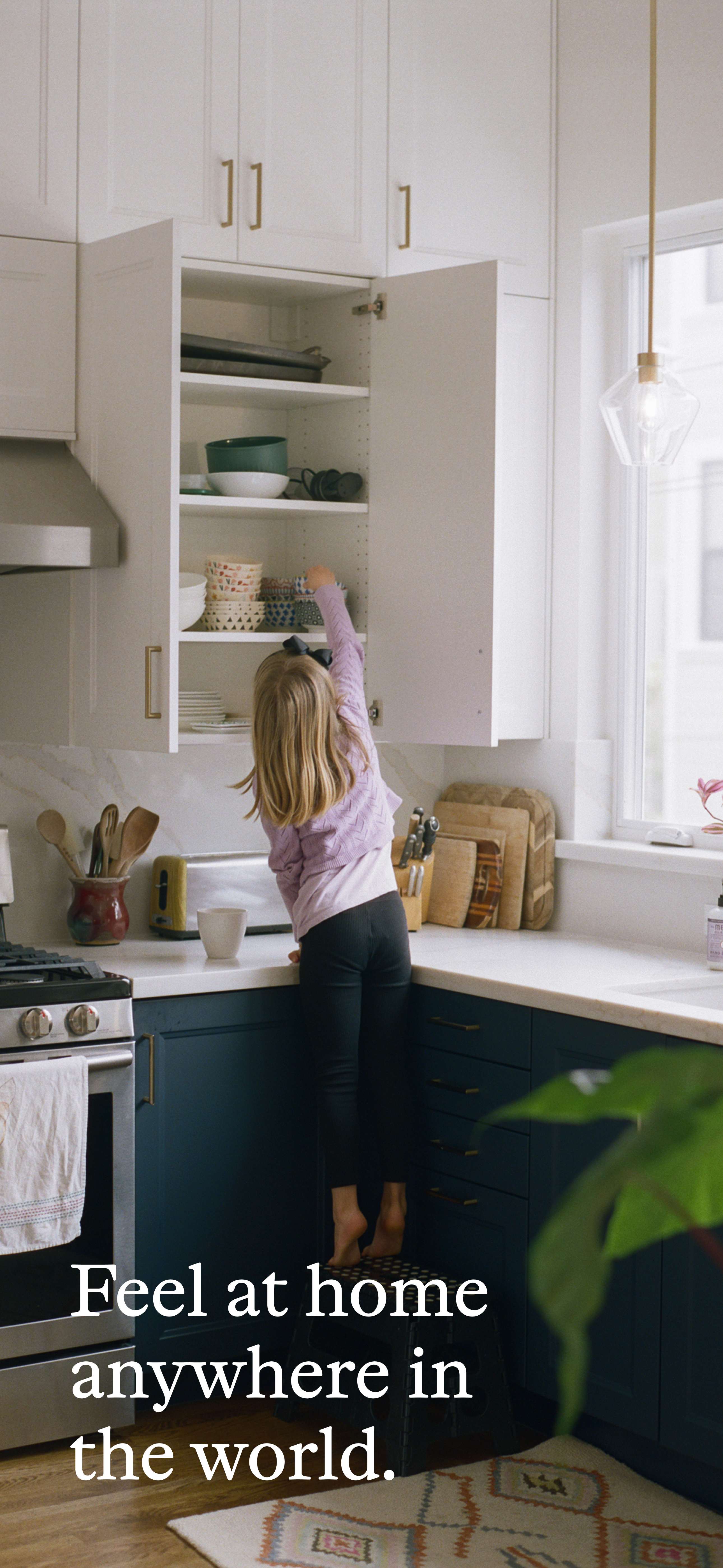 A girl reaching into a kitchen cabinet in a cozy, sunlit home—symbolizing the everyday comfort and belonging found through global house swapping with Kindred.